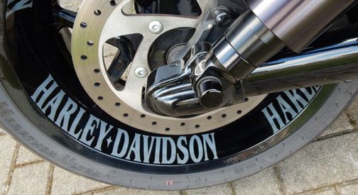 Nahaufnahme eines Harley-Davidson-Motorradrads mit polierter Bremsscheibe und markantem schwarzen Reifen mit weißer Aufschrift.